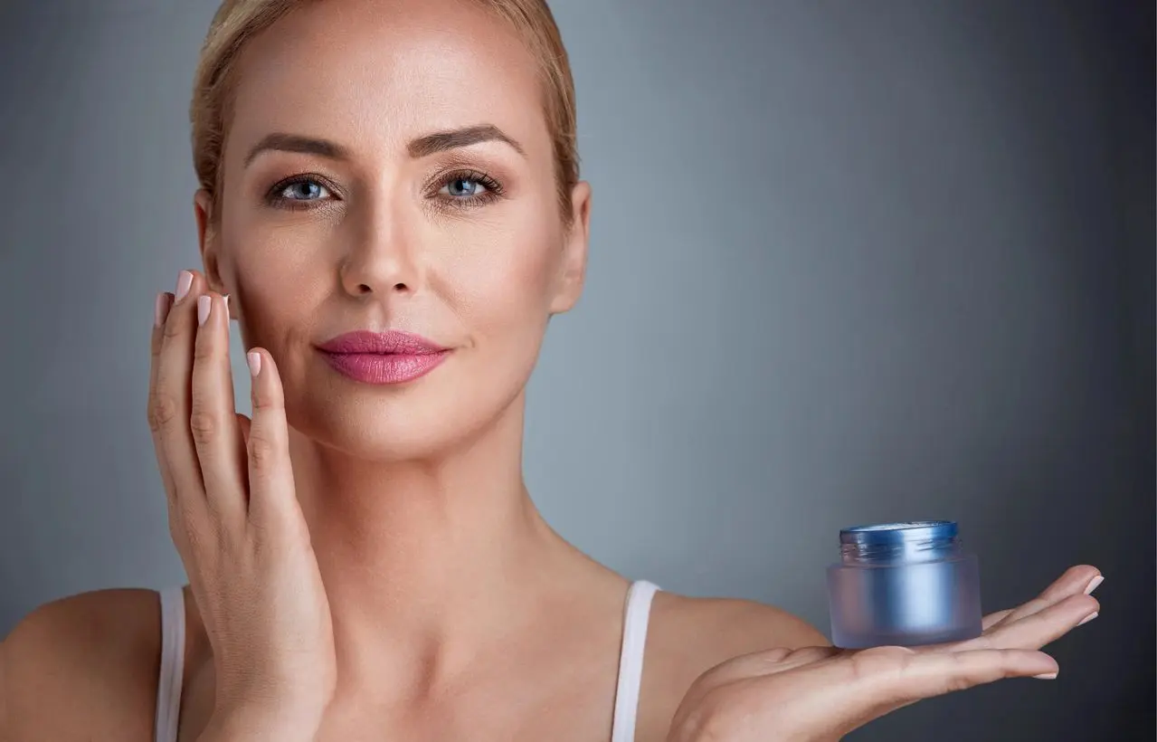 A woman holding up a jar of cream in front of her face.