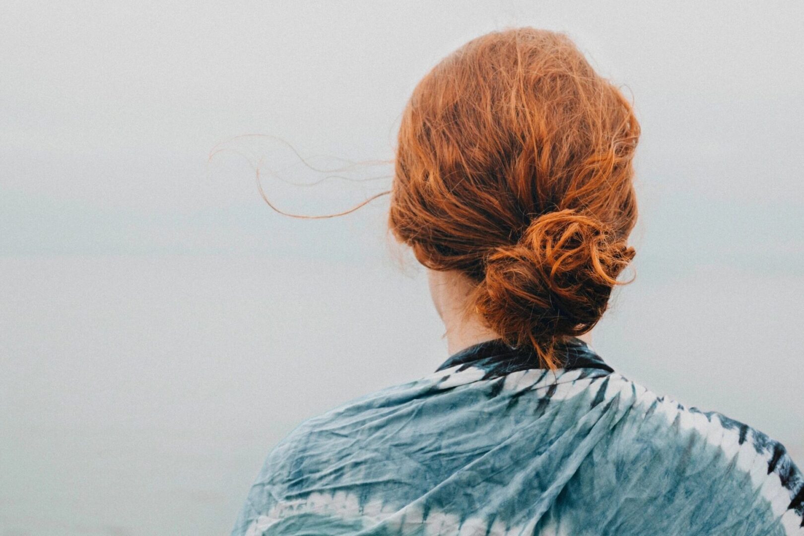 A woman with red hair is looking out at the ocean.